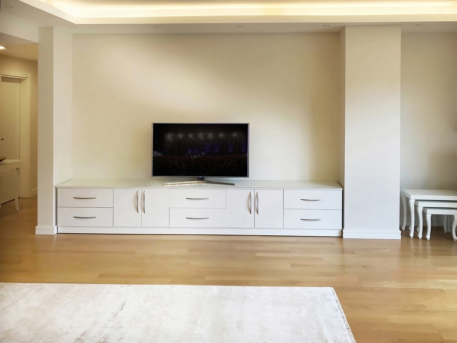 Modern, custom-made bookcase TV unit with a full wall of white wooden shelves, designed for spacious and stylish storage.  