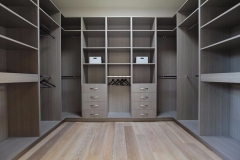 Custom-made spacious walk-in closet with full-wall wooden shelving in a light natural color, providing ample storage.  